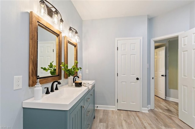 bathroom with a sink, double vanity, wood finished floors, and baseboards