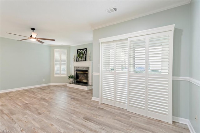 unfurnished living room featuring ceiling fan, a high end fireplace, visible vents, baseboards, and light wood finished floors