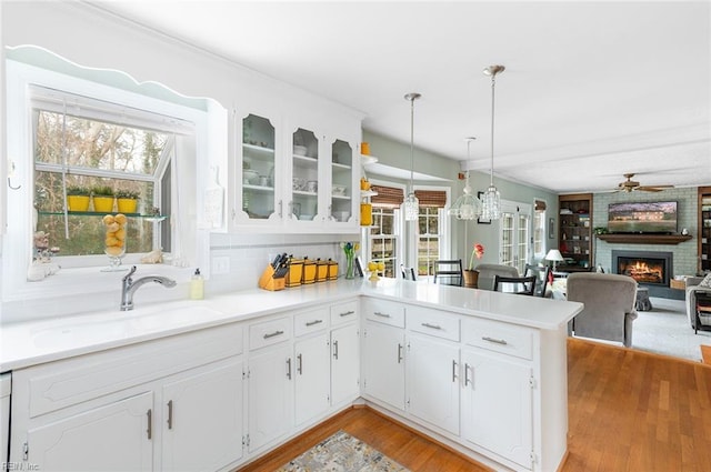 kitchen with light countertops, hanging light fixtures, glass insert cabinets, a sink, and a peninsula