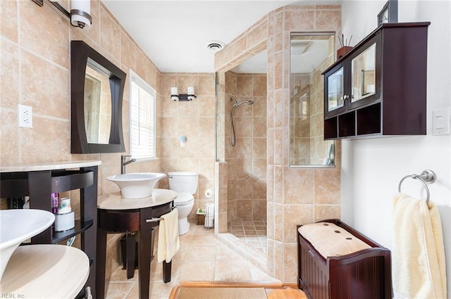 full bathroom with tile walls, visible vents, toilet, a shower stall, and tile patterned floors