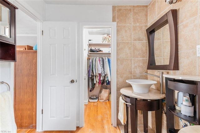 bathroom featuring wood finished floors, tile walls, vanity, and a spacious closet