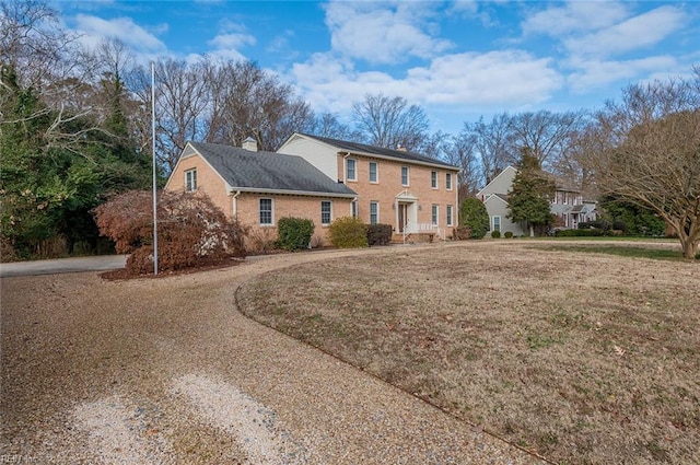 colonial-style house with a front yard, brick siding, driveway, and a chimney