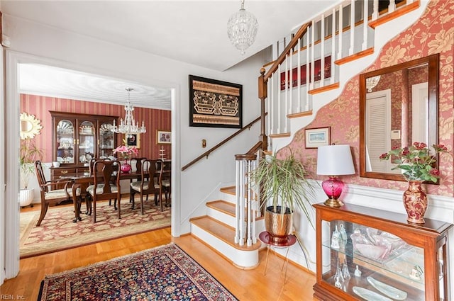 stairs with an inviting chandelier, wallpapered walls, and wood finished floors