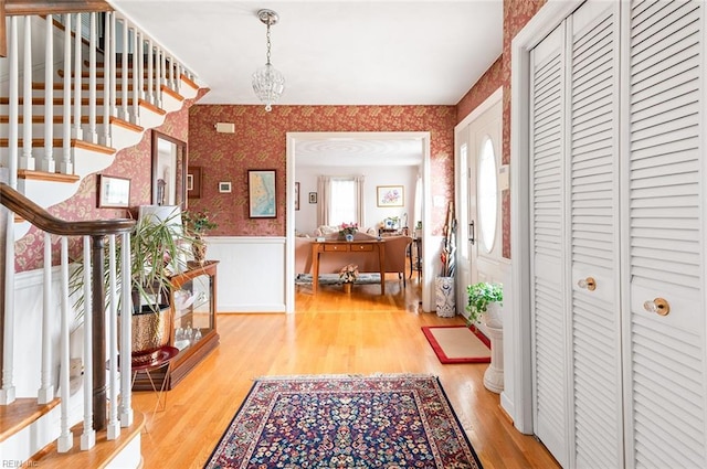 foyer with light wood-type flooring, wallpapered walls, stairway, and wainscoting