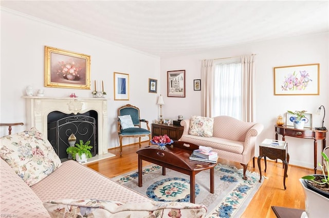 living area with a fireplace with raised hearth, light wood finished floors, and crown molding