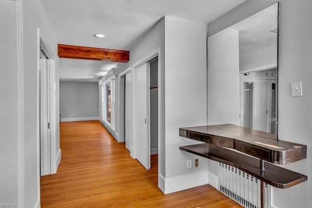 corridor featuring beam ceiling, radiator, light wood-style flooring, and baseboards