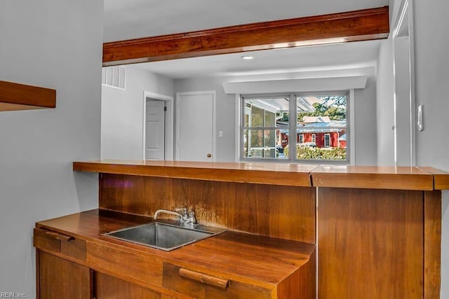 bar with wet bar, beam ceiling, visible vents, and a sink