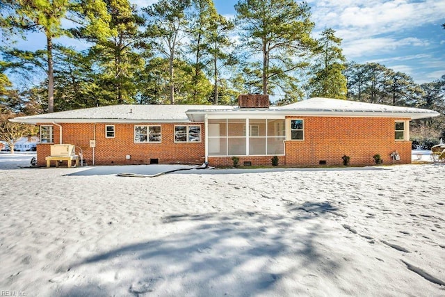 snow covered property with crawl space, brick siding, and a chimney