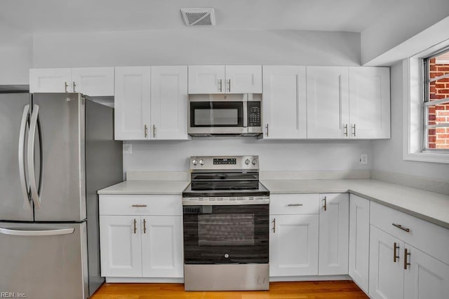 kitchen with stainless steel appliances, light countertops, visible vents, light wood-style floors, and white cabinets