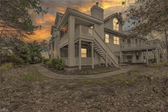 back of property at dusk featuring a chimney and stairs