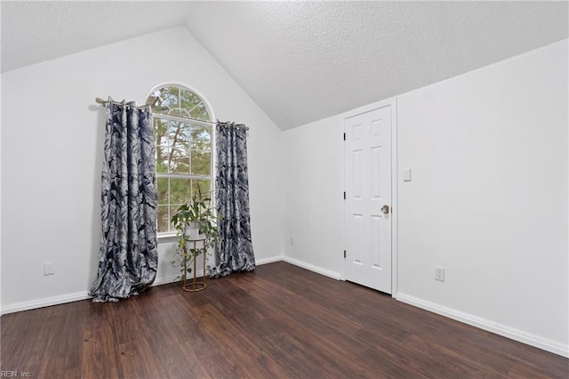 empty room with dark wood-style floors, a textured ceiling, lofted ceiling, and baseboards