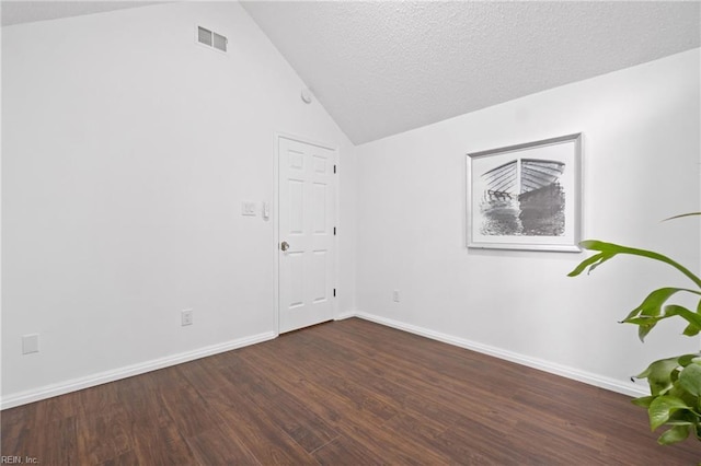 spare room featuring a textured ceiling, dark wood-style flooring, visible vents, baseboards, and vaulted ceiling