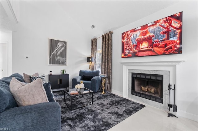 living room with vaulted ceiling, visible vents, a high end fireplace, and baseboards