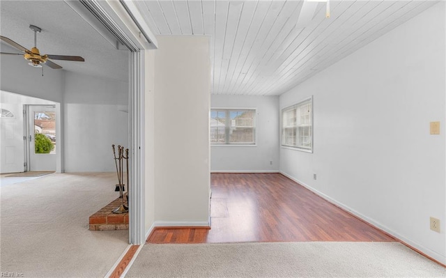 spare room with baseboards, a ceiling fan, light colored carpet, wooden ceiling, and light wood-type flooring