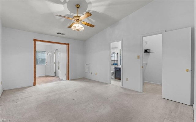 unfurnished bedroom featuring ensuite bathroom, light carpet, visible vents, vaulted ceiling, and a walk in closet