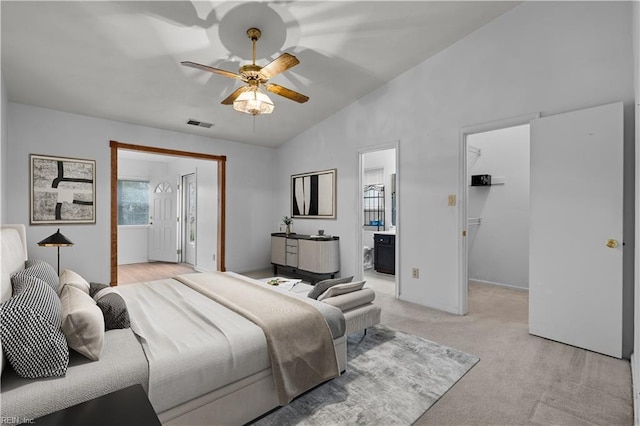 bedroom with a walk in closet, visible vents, light carpet, vaulted ceiling, and ensuite bath