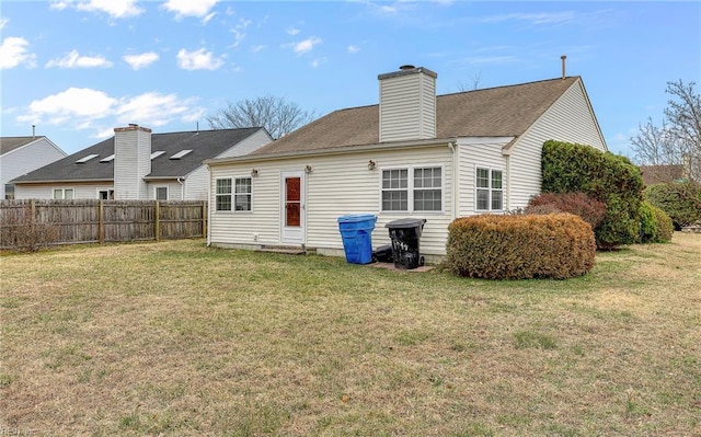 back of house featuring a shingled roof, a lawn, a chimney, and fence