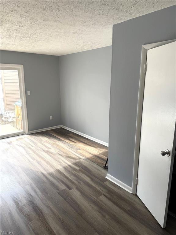 spare room featuring dark wood-type flooring, a textured ceiling, and baseboards