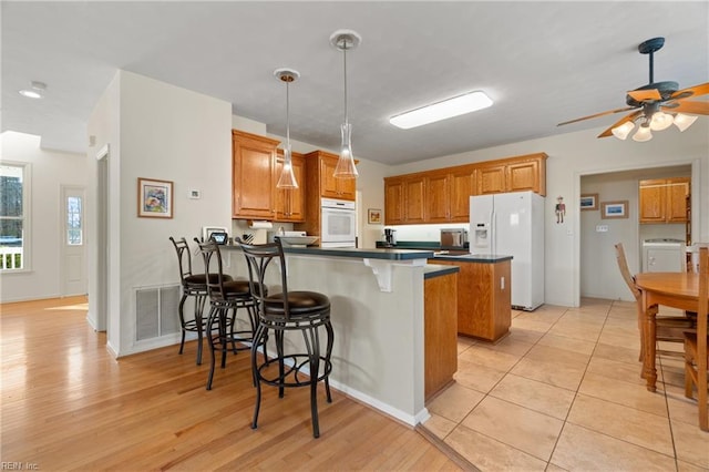 kitchen featuring a breakfast bar, white refrigerator with ice dispenser, dark countertops, washer / dryer, and a peninsula