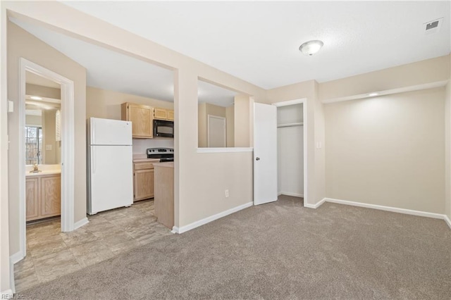 interior space featuring black microwave, light brown cabinets, light carpet, electric stove, and freestanding refrigerator