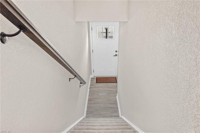 stairs featuring baseboards, wood finished floors, and a textured wall