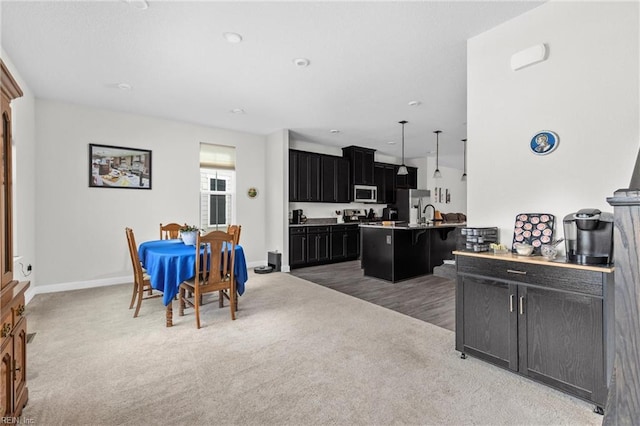 kitchen featuring a breakfast bar area, dark cabinets, appliances with stainless steel finishes, a center island with sink, and pendant lighting