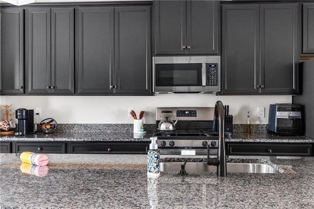 kitchen with dark stone counters, appliances with stainless steel finishes, a sink, and dark cabinets