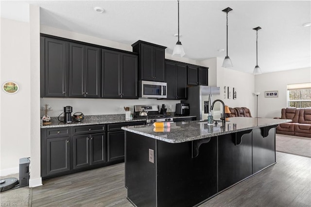 kitchen featuring appliances with stainless steel finishes, a kitchen breakfast bar, a kitchen island with sink, dark cabinetry, and pendant lighting