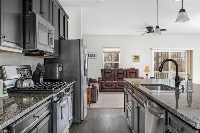 kitchen featuring a sink, hanging light fixtures, appliances with stainless steel finishes, dark cabinetry, and dark stone countertops