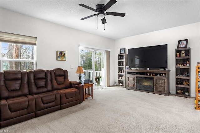 living area featuring a textured ceiling, light carpet, a glass covered fireplace, and a wealth of natural light