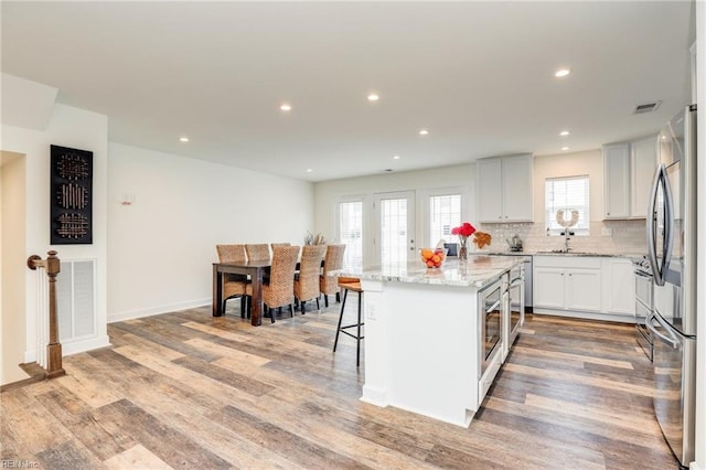 kitchen featuring visible vents, light stone counters, a center island, light wood-type flooring, and white cabinetry