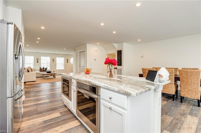 kitchen with white cabinets, appliances with stainless steel finishes, open floor plan, light stone counters, and a center island