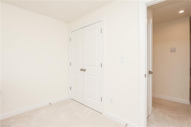 unfurnished bedroom featuring a closet, light colored carpet, and baseboards