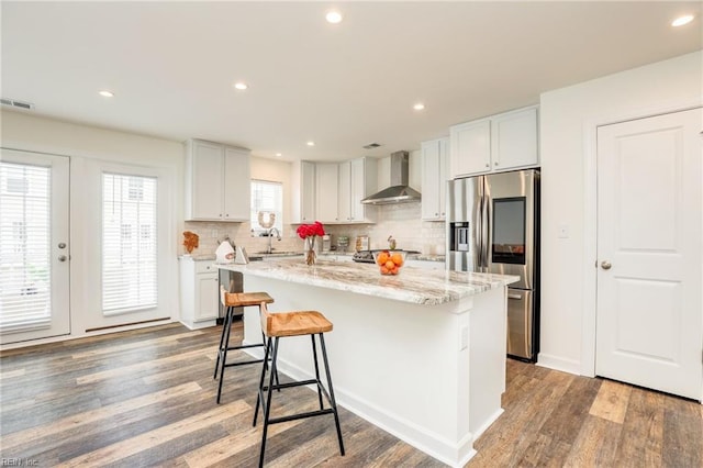 kitchen featuring white cabinets, stainless steel fridge, a kitchen island, and wall chimney exhaust hood