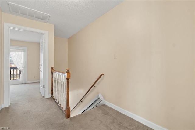 hallway featuring baseboards, visible vents, light carpet, and an upstairs landing