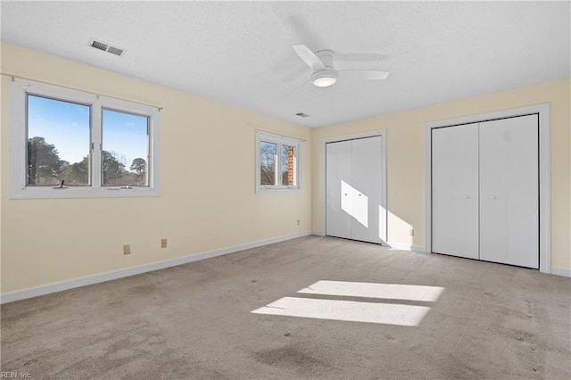 unfurnished bedroom featuring ceiling fan, light colored carpet, visible vents, baseboards, and multiple closets