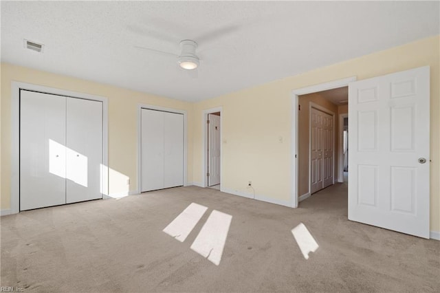 unfurnished bedroom with multiple closets, light colored carpet, visible vents, a ceiling fan, and baseboards