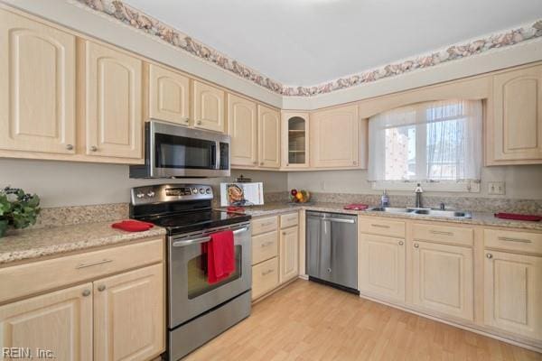 kitchen featuring appliances with stainless steel finishes, a sink, glass insert cabinets, and light wood-style floors