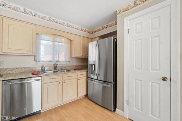 kitchen with a sink, light countertops, appliances with stainless steel finishes, light brown cabinetry, and light wood finished floors