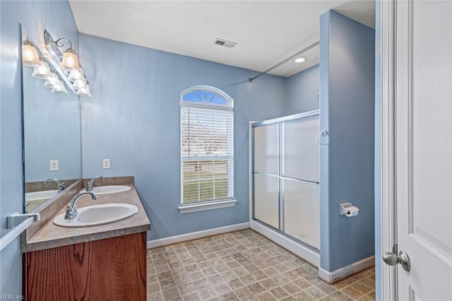 bathroom featuring double vanity, visible vents, a sink, a shower stall, and baseboards