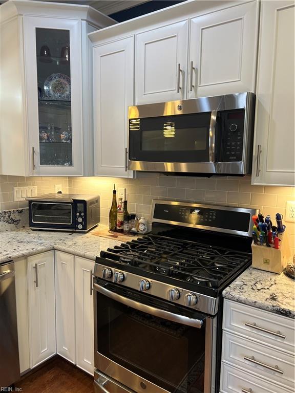 kitchen featuring glass insert cabinets, tasteful backsplash, white cabinetry, and stainless steel appliances