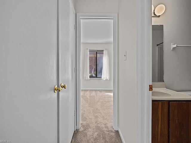 hallway featuring light colored carpet, a sink, and baseboards