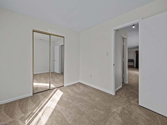 unfurnished bedroom featuring a closet, light colored carpet, and baseboards