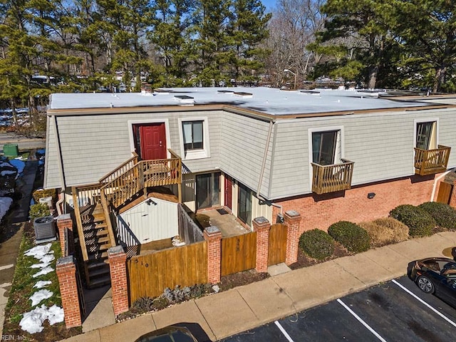 view of front facade with a fenced front yard, brick siding, uncovered parking, central AC, and stairs