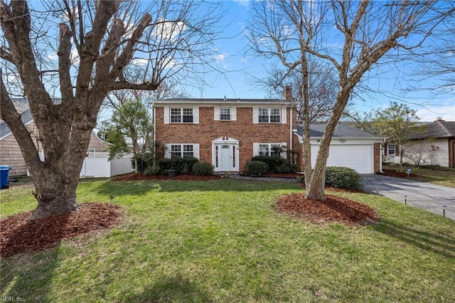 colonial home featuring driveway, fence, a front yard, an attached garage, and a chimney