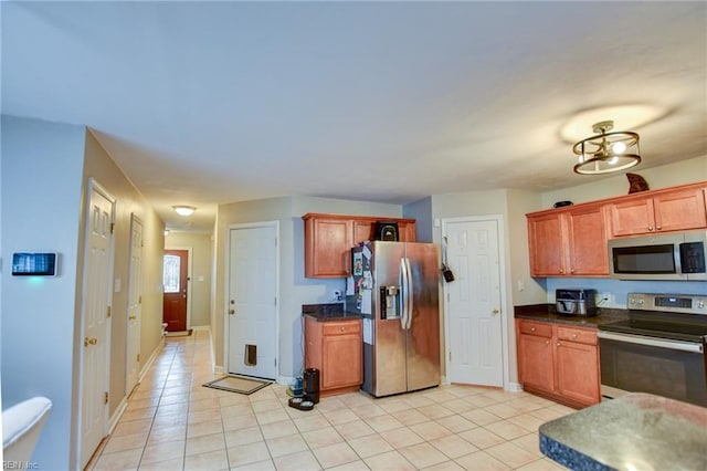 kitchen with light tile patterned floors, appliances with stainless steel finishes, brown cabinetry, and dark countertops