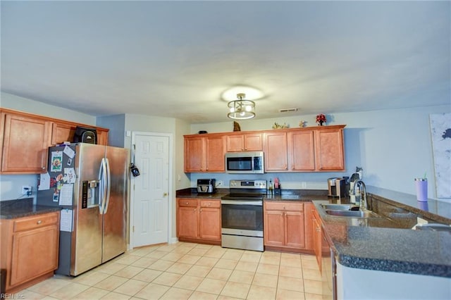 kitchen with appliances with stainless steel finishes, dark countertops, a sink, and brown cabinets