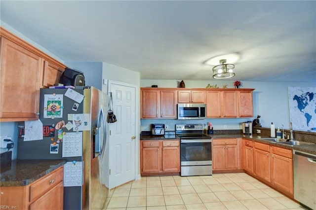 kitchen with appliances with stainless steel finishes, brown cabinetry, a sink, and light tile patterned flooring