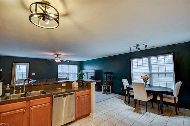 kitchen featuring a sink, stainless steel dishwasher, brown cabinets, dark countertops, and plenty of natural light