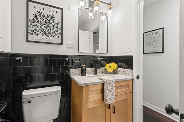 half bathroom featuring toilet, a wainscoted wall, wood finished floors, vanity, and tile walls